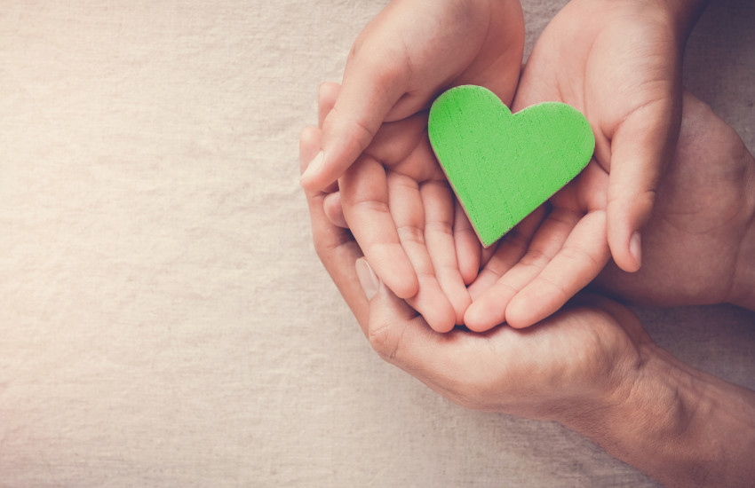 Cartoncino a forma di cuore verde tra le mani